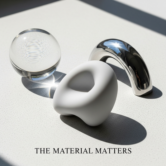 A minimalist flat lay of body-safe sex toy materials: velvety silicone, clear glass, and polished steel, illustrating the ultimate guide to body-safe sex toy materials.