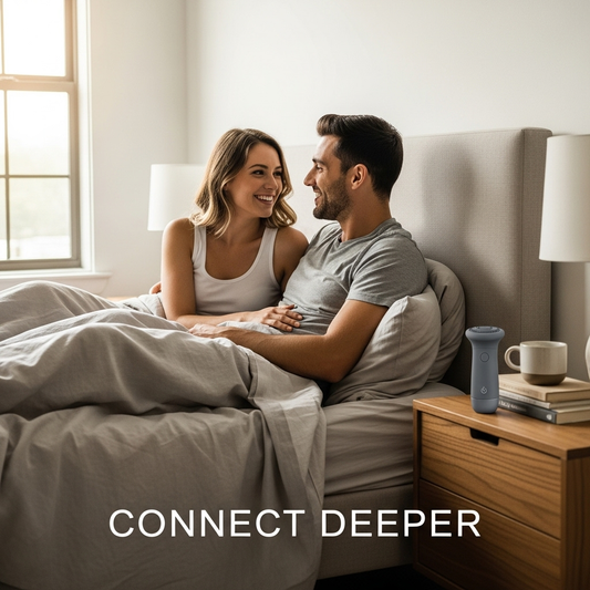 A smiling couple in bed looking at each other, representing the communication needed to use a vibrator with a partner, with a sleek toy on the nightstand.